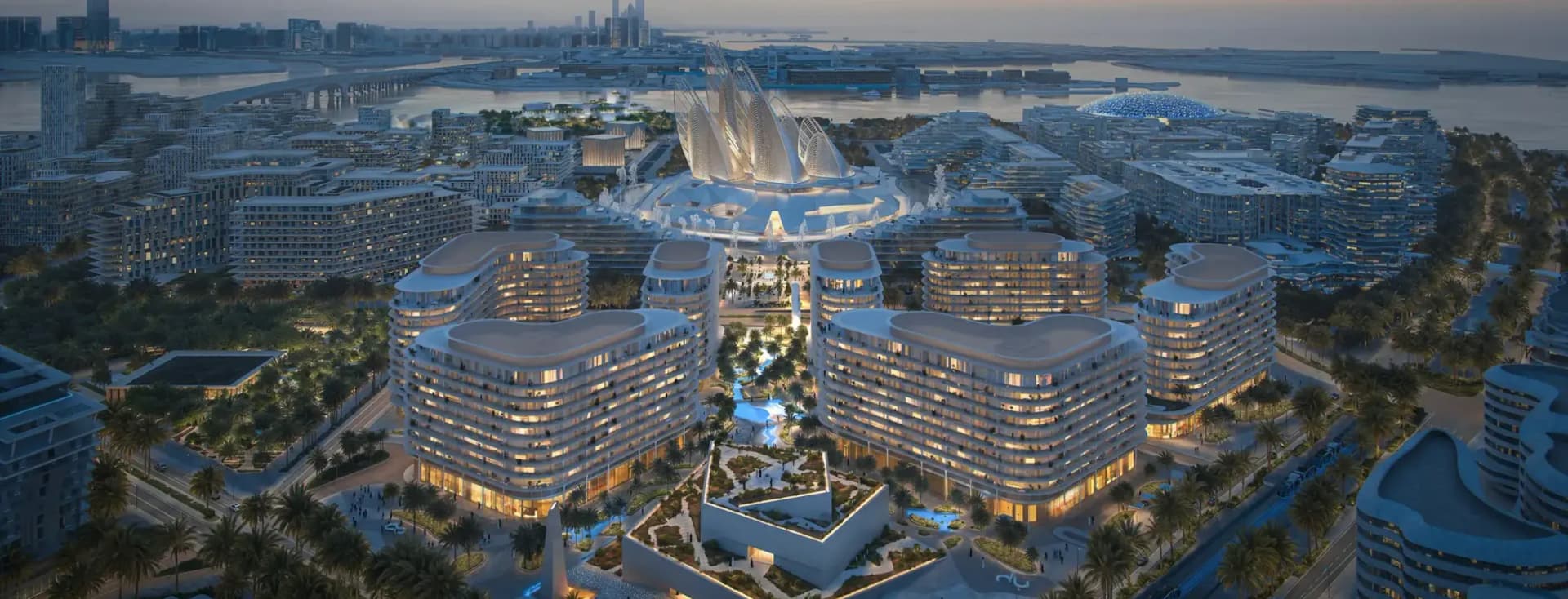 Aerial view of a futuristic cityscape at dusk with illuminated, curvy modern buildings, lush greenery, and waterfront in the background.