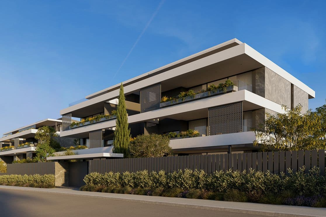 Modern three-story apartment building with wide terraces, planter boxes and greenery, minimalist white and gray facade under clear blue sky.