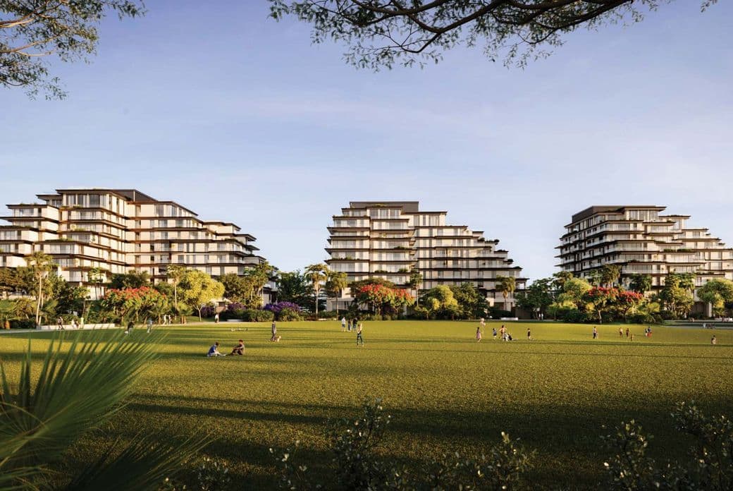 Modern, tiered buildings surrounded by lush greenery and an open lawn with people relaxing under a clear blue sky.