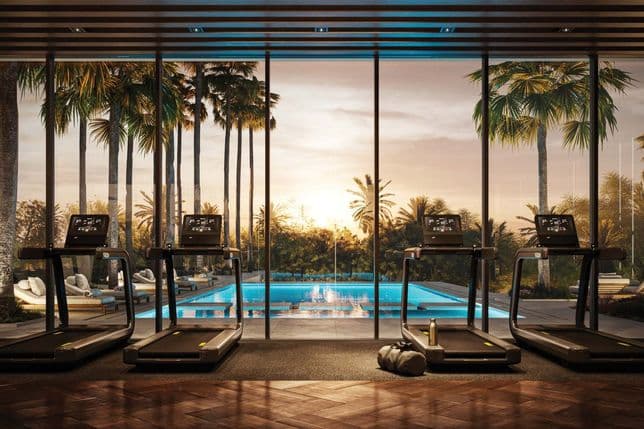 Four treadmills face a large window overlooking a pool and palm trees at sunset, creating a serene and inviting gym atmosphere.