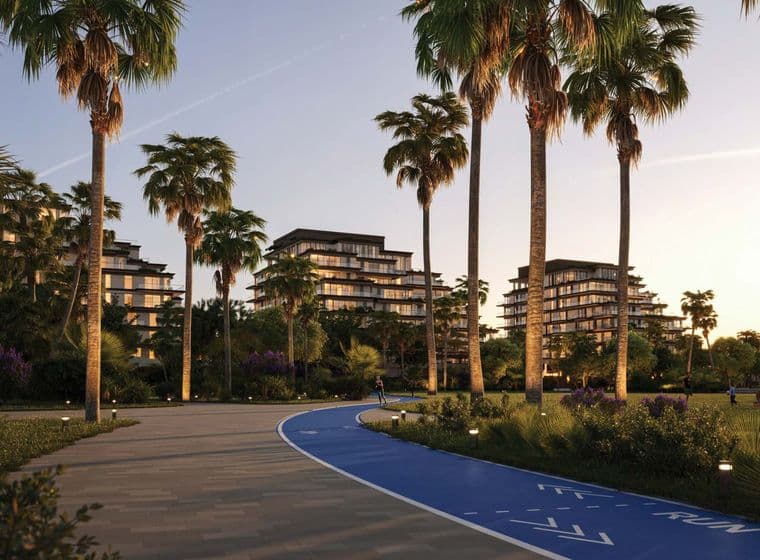 Pathway lined with palm trees, adjacent to modern buildings at sunset. A blue running track is visible on the right.