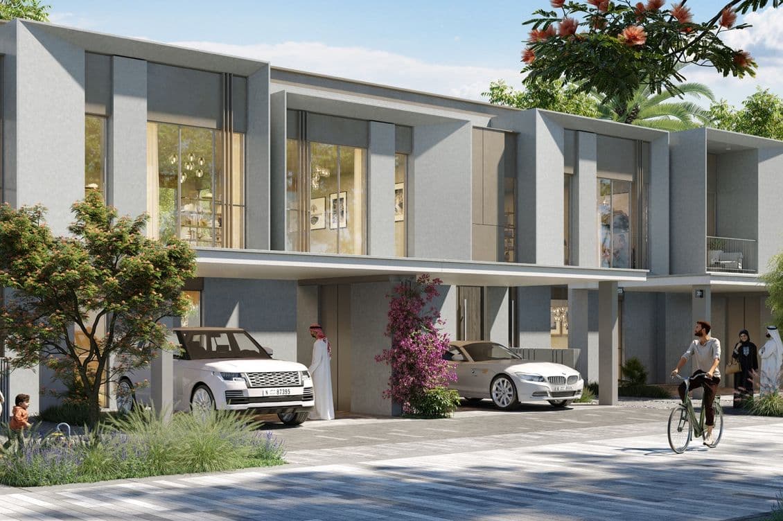 Modern townhouse with large windows, cars in driveways, lush greenery, and people walking and cycling on a sunny day.