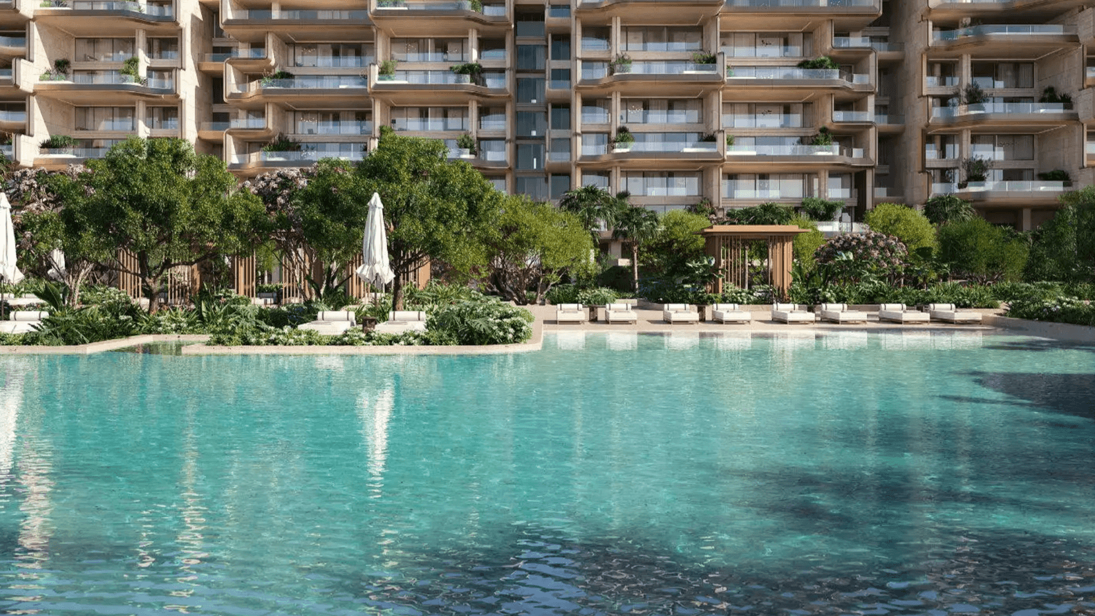 Luxurious waterfront apartments with balconies overlooking a large, clear swimming pool surrounded by lush greenery and sun loungers.