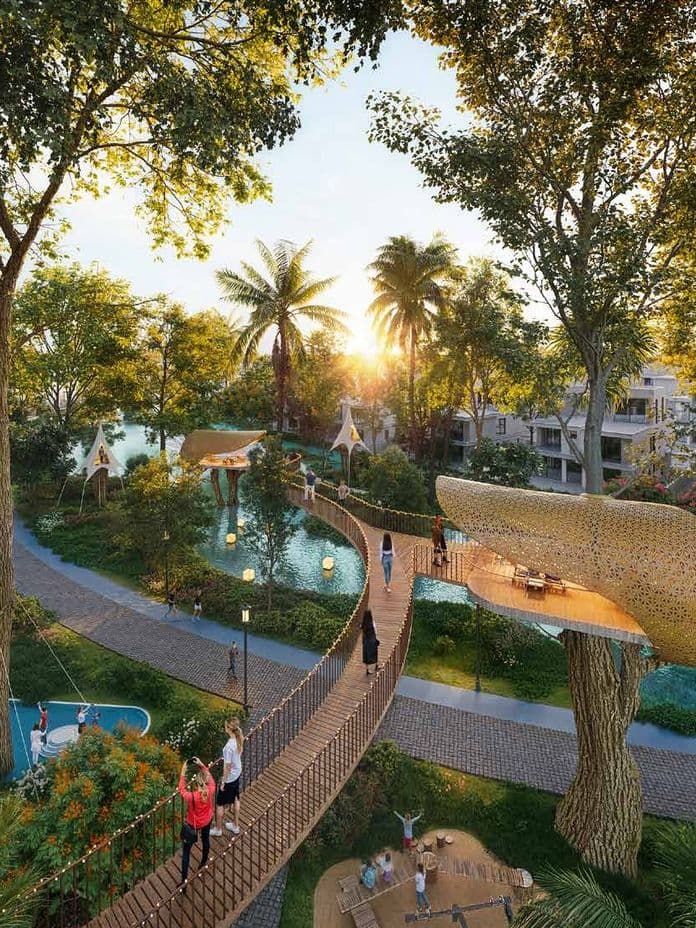 Lush park with treehouses, play areas, winding paths, and water features at sunset, surrounded by greenery and modern buildings.