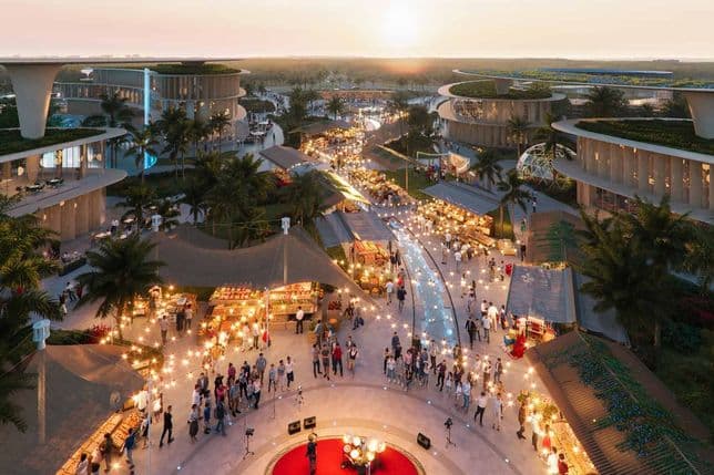 Aerial view of a vibrant outdoor market at sunset, with people, stalls, string lights, palm trees, and modern buildings in the background.