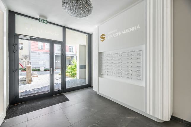 Světlá vstupní hala s poštovními schránkami, nápisem „Rezidence Staropramenná“, šedou dlažbou a prosklenými dveřmi s výhledem do dvora.