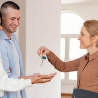 Un agente immobiliare consegna le chiavi a una coppia sorridente in una casa moderna e luminosa.
