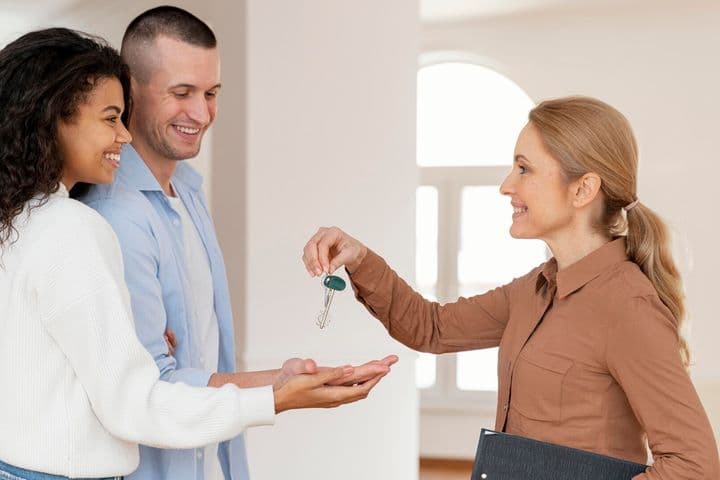 Un agente immobiliare consegna le chiavi a una coppia sorridente in una casa moderna e luminosa.