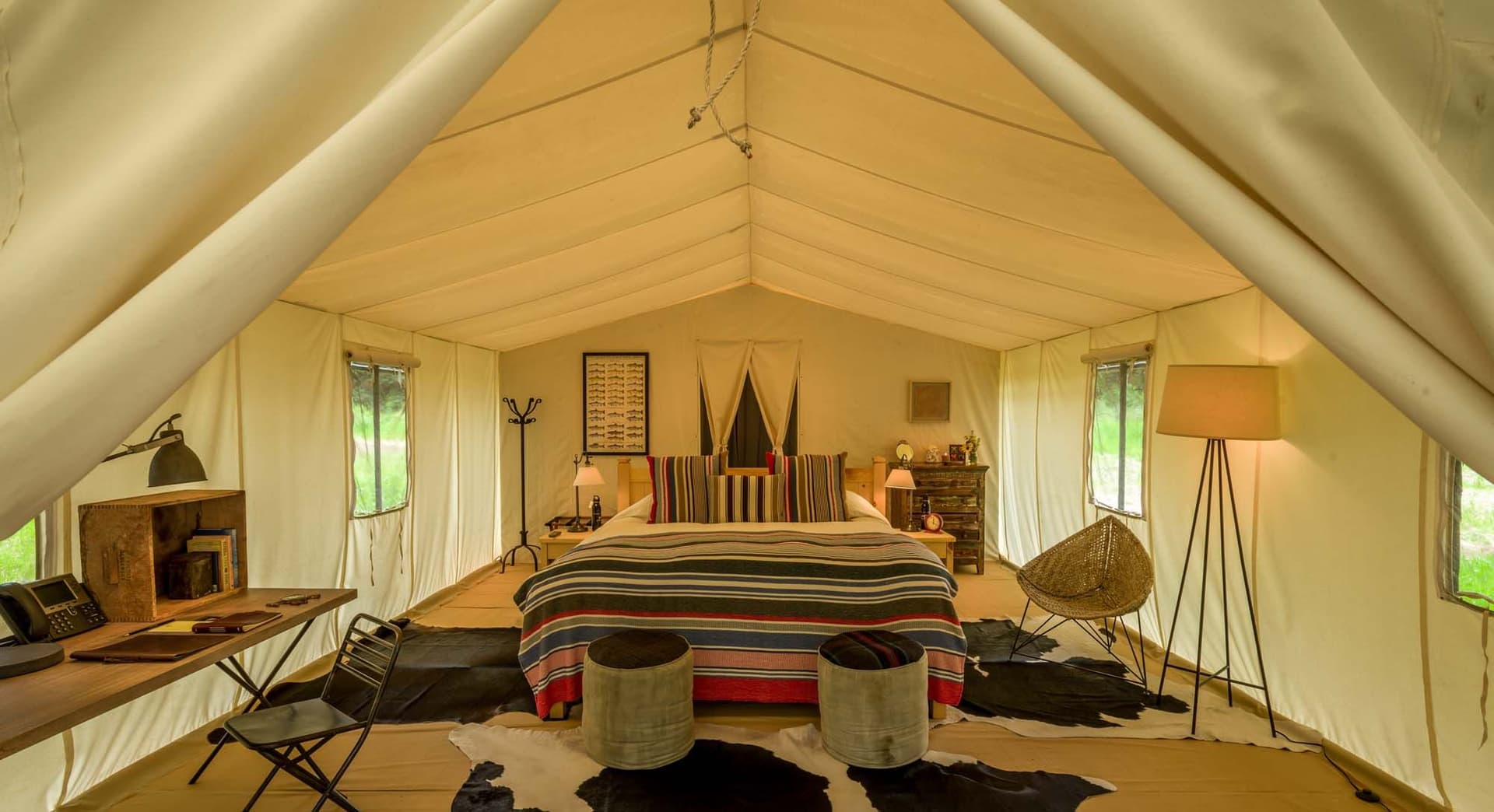 Luxurious glamping tent interior with a cozy bed, striped bedding, cowhide rugs, and warm lighting, creating a rustic yet elegant atmosphere.