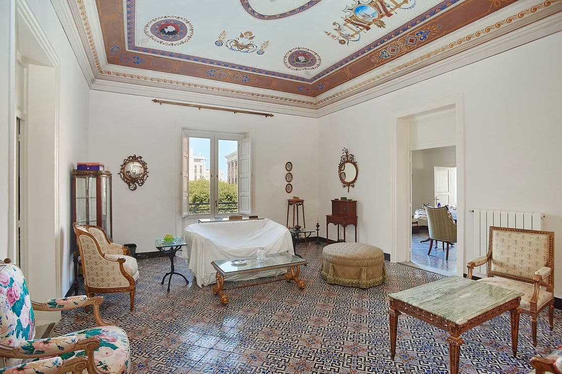 Elegant living room with ornate ceiling, vintage furniture, patterned tile floor, and large window overlooking greenery.