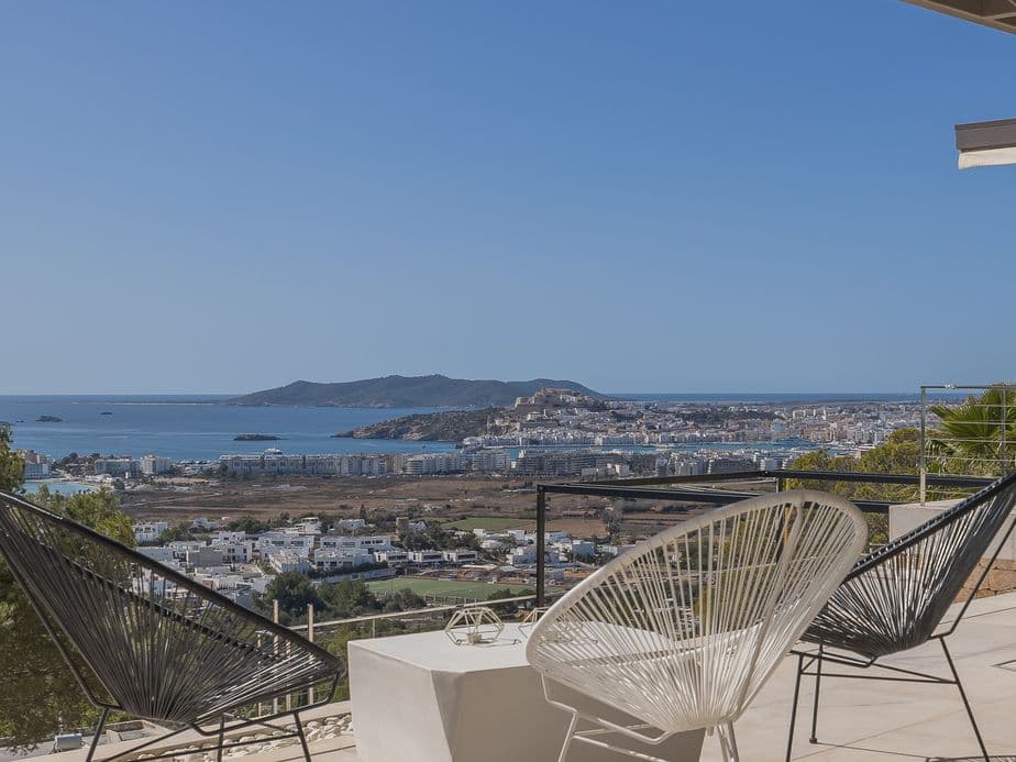 Terrace with designer chairs overlooking Ibiza Town, the sea, and surrounding landscape under a clear blue sky.