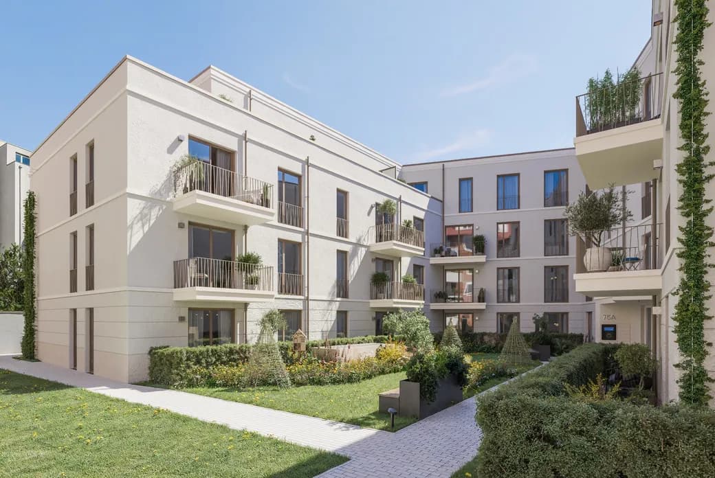 Sunlit beige apartment complex with multiple balconies, a manicured garden, and ivy-clad walls under a clear blue sky.