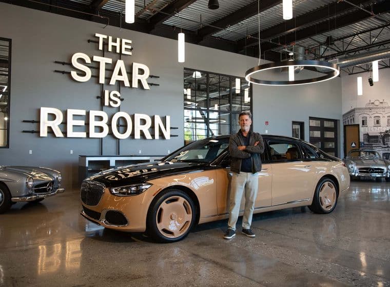 A man stands proudly in front of a two-tone Maybach sedan in a showroom. "The Star is Reborn" is lit up on the wall behind him.