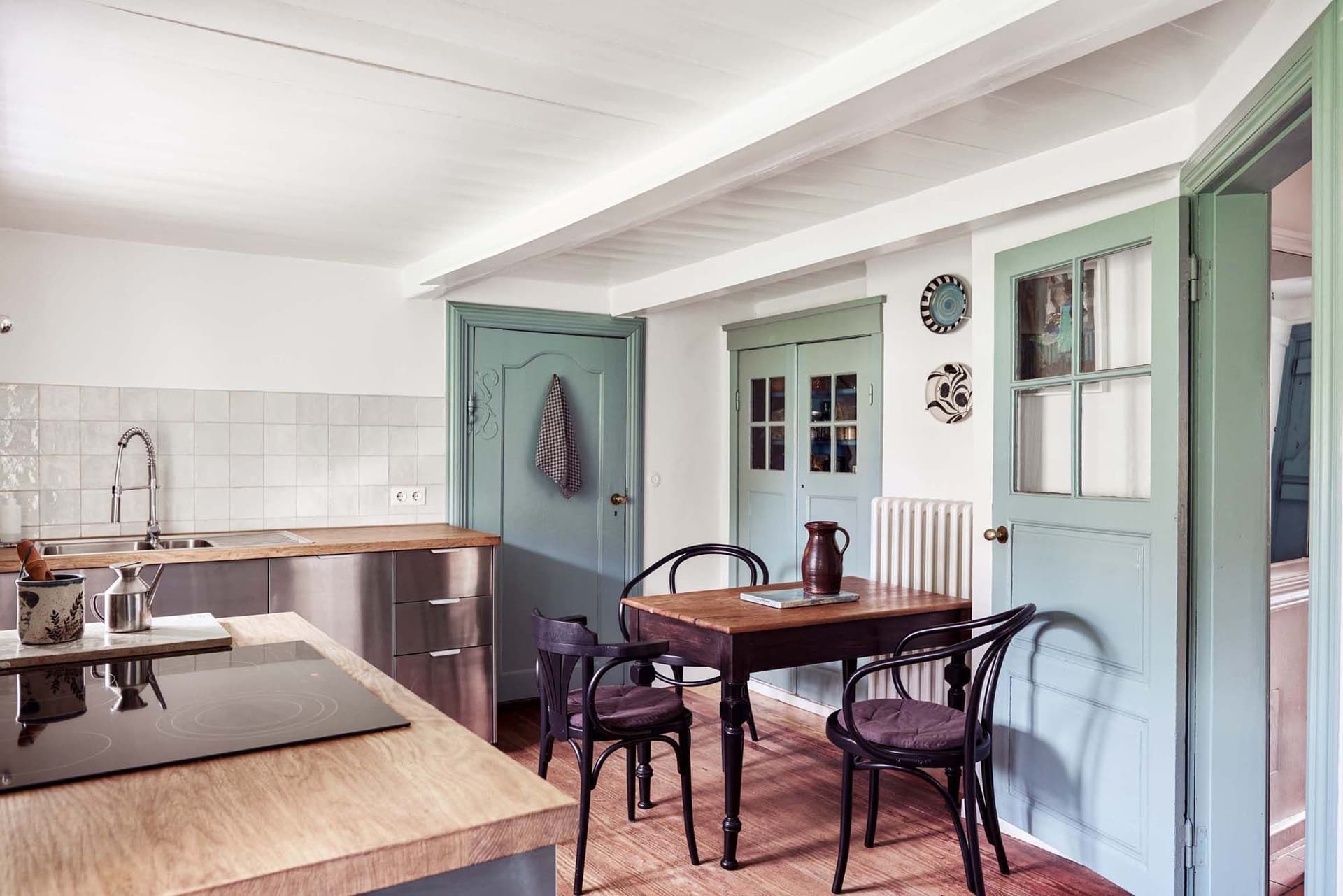 Cozy kitchen with wooden table, black chairs, mint green doors, tiled backsplash, and modern appliances. Bright and inviting atmosphere.