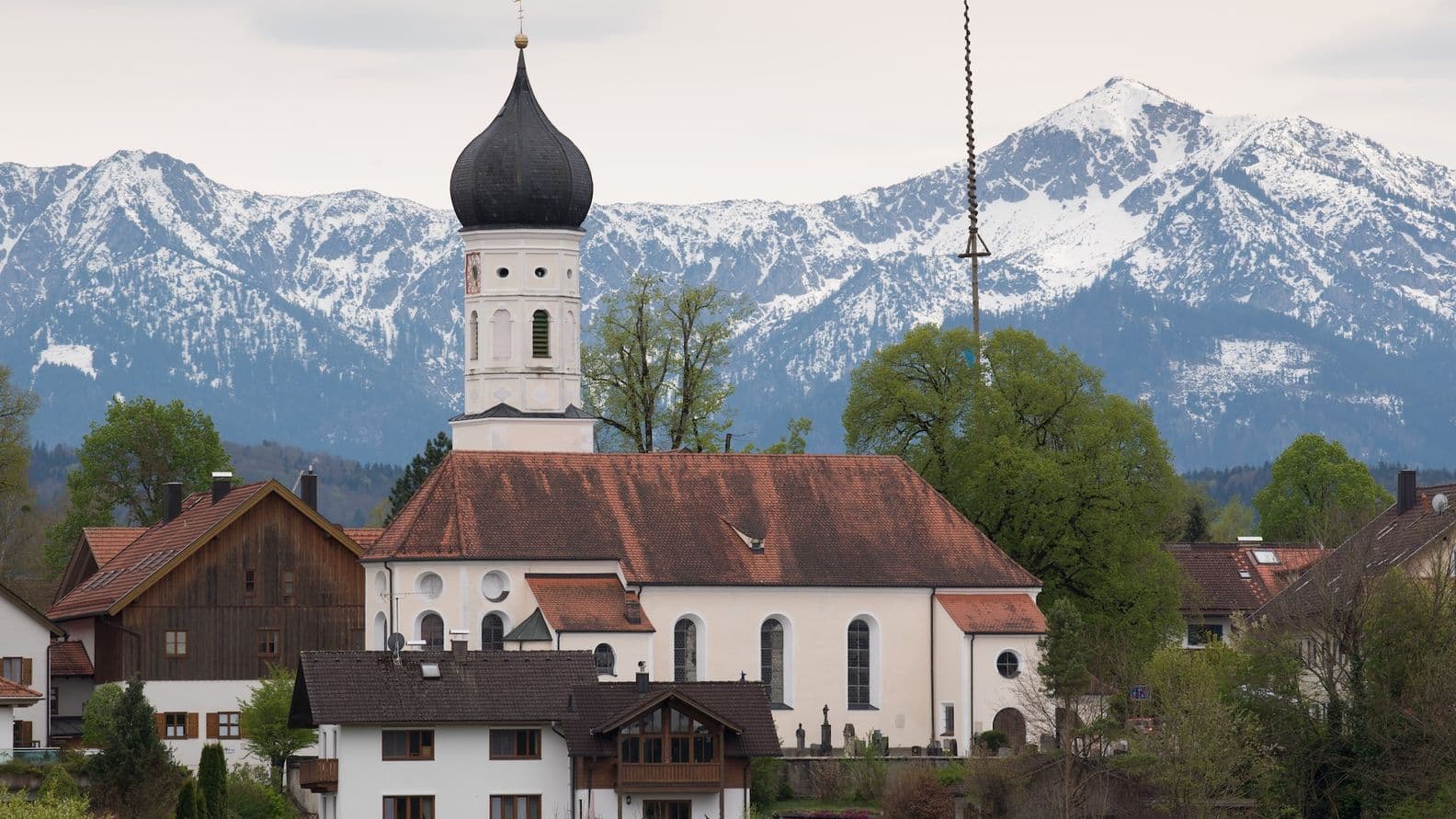 Bavarian church in Iffeldorf with distinctive onion dome and the Alps in the background – a scenic location for residential living