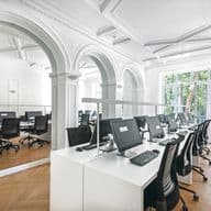 Bright, modern office space with rows of computers on white desks, large windows, and decorative arches.