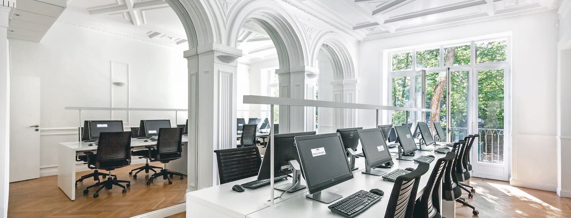 Bright, modern office space with rows of computers on white desks, large windows, and decorative arches.