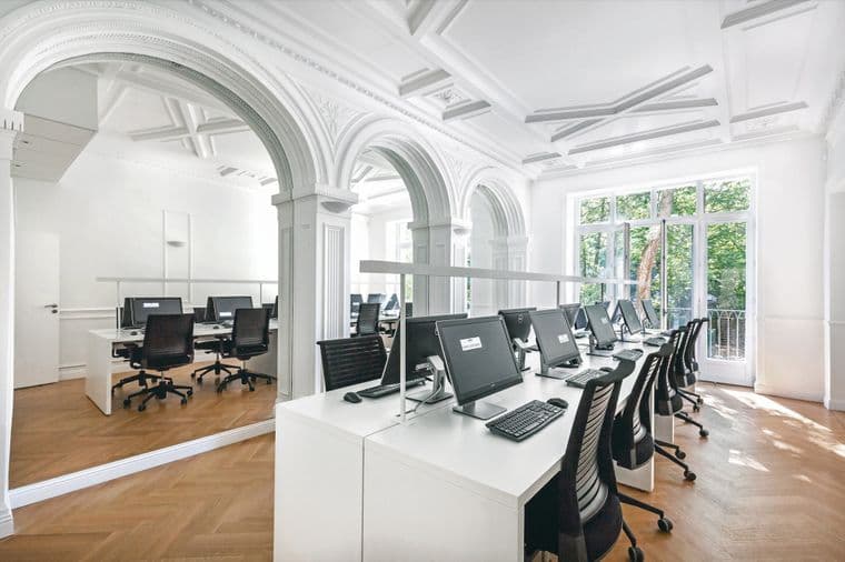 Bright, modern office space with rows of computers on white desks, large windows, and decorative arches.