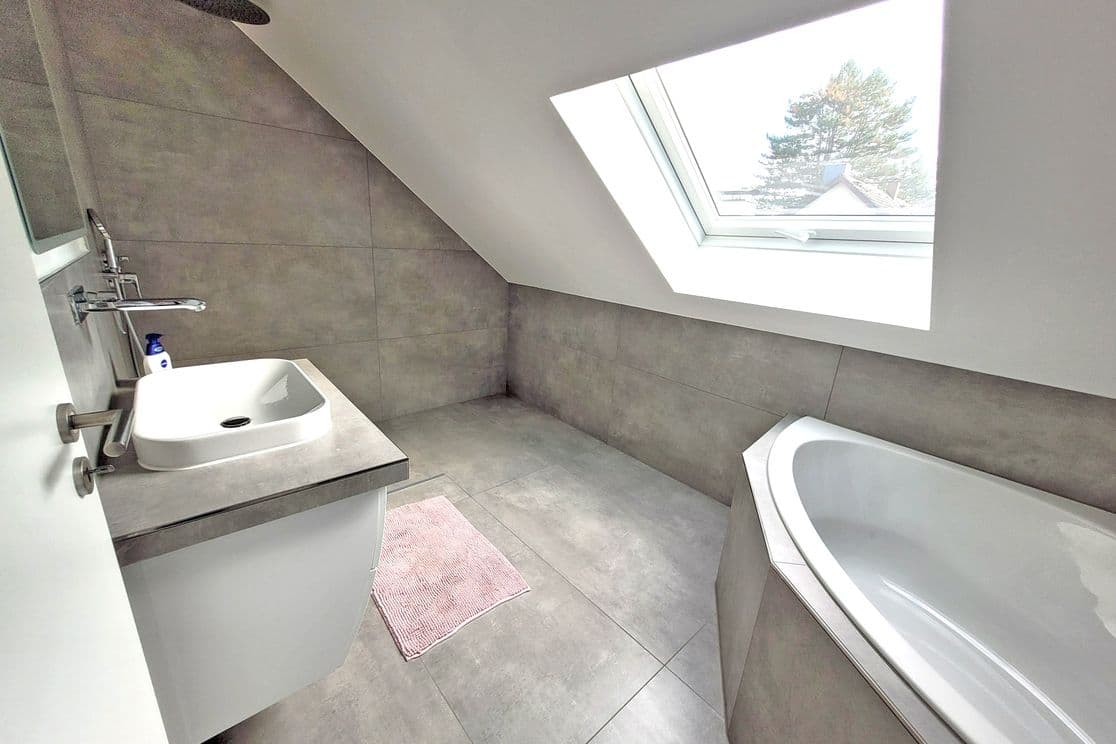 Modernized attic bathroom with grey tiles, freestanding bathtub, walk-in rain shower and large skylight window