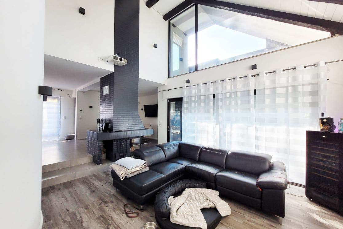 Bright and open-plan living room with modern black fireplace, floor-to-ceiling windows and leather sectional sofa