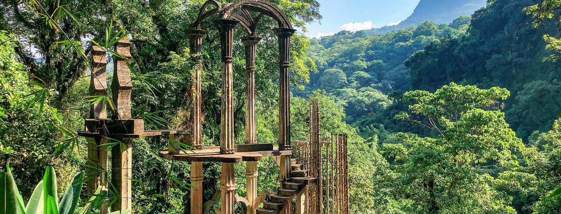 A surreal garden with lush jungle, enchanted sculptures and mystical concrete structures in Las Pozas, Mexico.