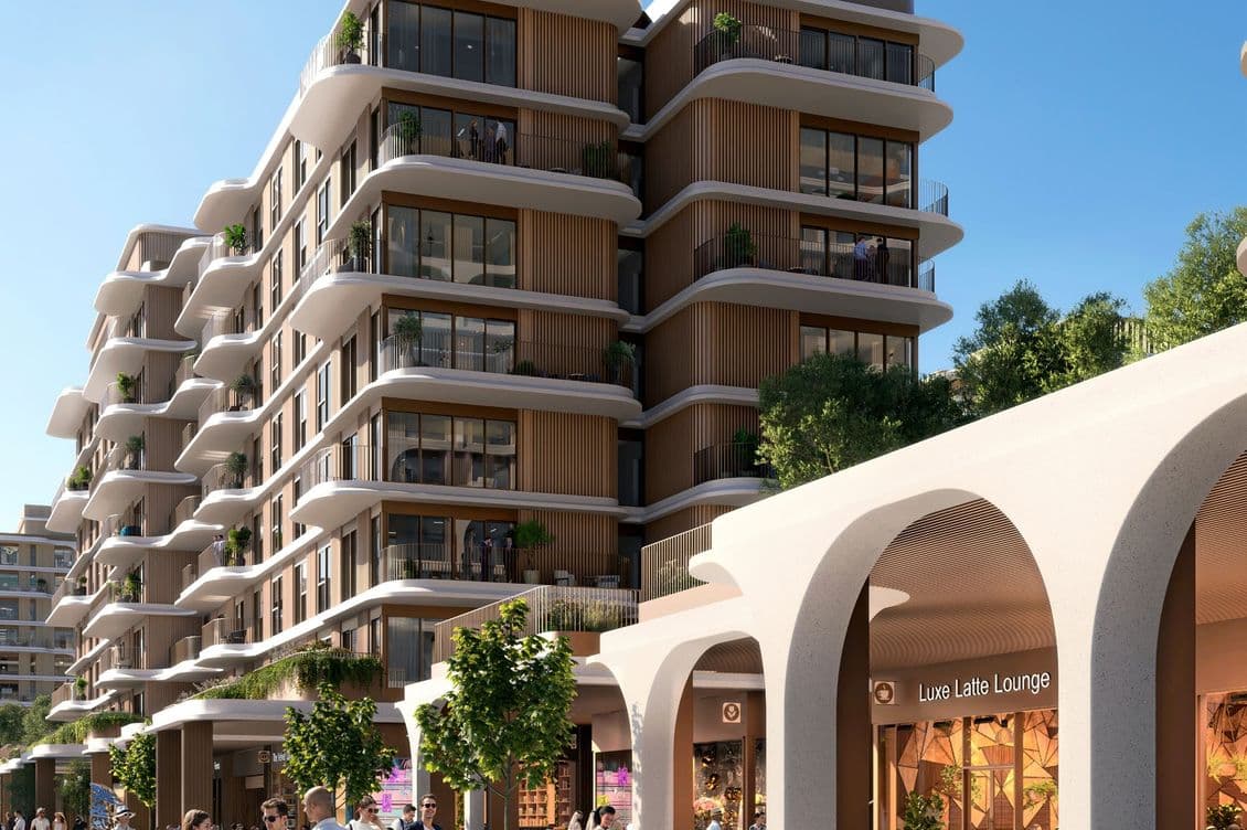 Street-level view of The Beach House Fahid with boutique retail including “Luxe Latte Lounge,” curved modern architecture, and people enjoying the outdoor promenade under clear blue skies.