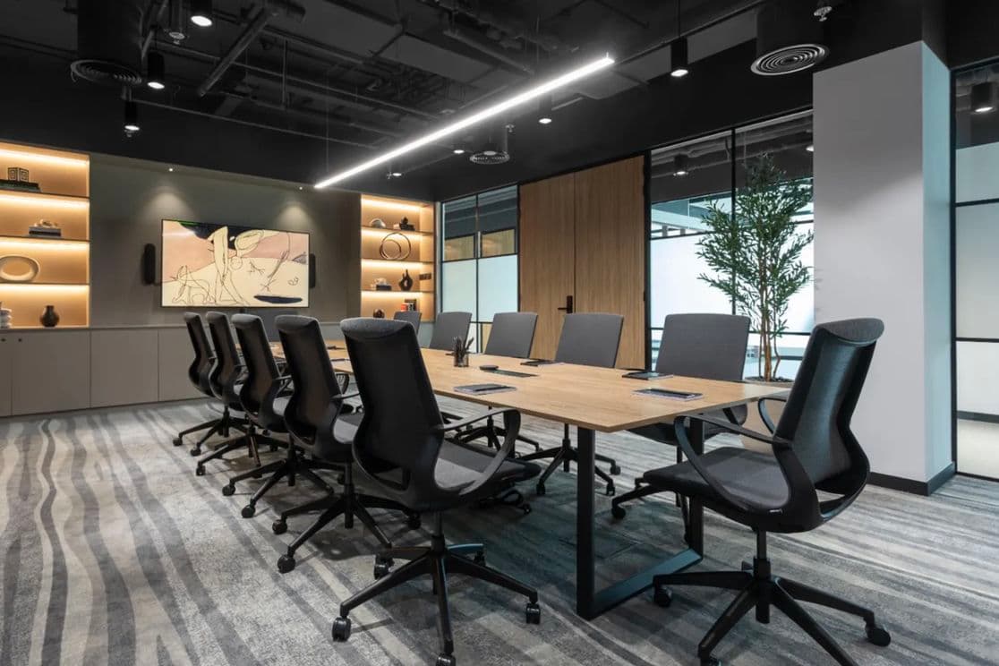 Modern conference room with a long wooden table, black swivel chairs, shelves with decor, and a large artwork on the wall.