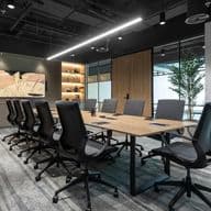 Modern conference room with a long wooden table, black swivel chairs, shelves with decor, and a large artwork on the wall.