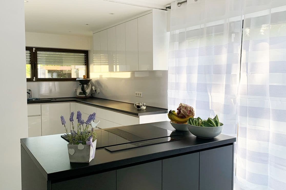 Bright, contemporary kitchen with a black cooking island, white high-gloss cabinetry and large window with sheer curtains