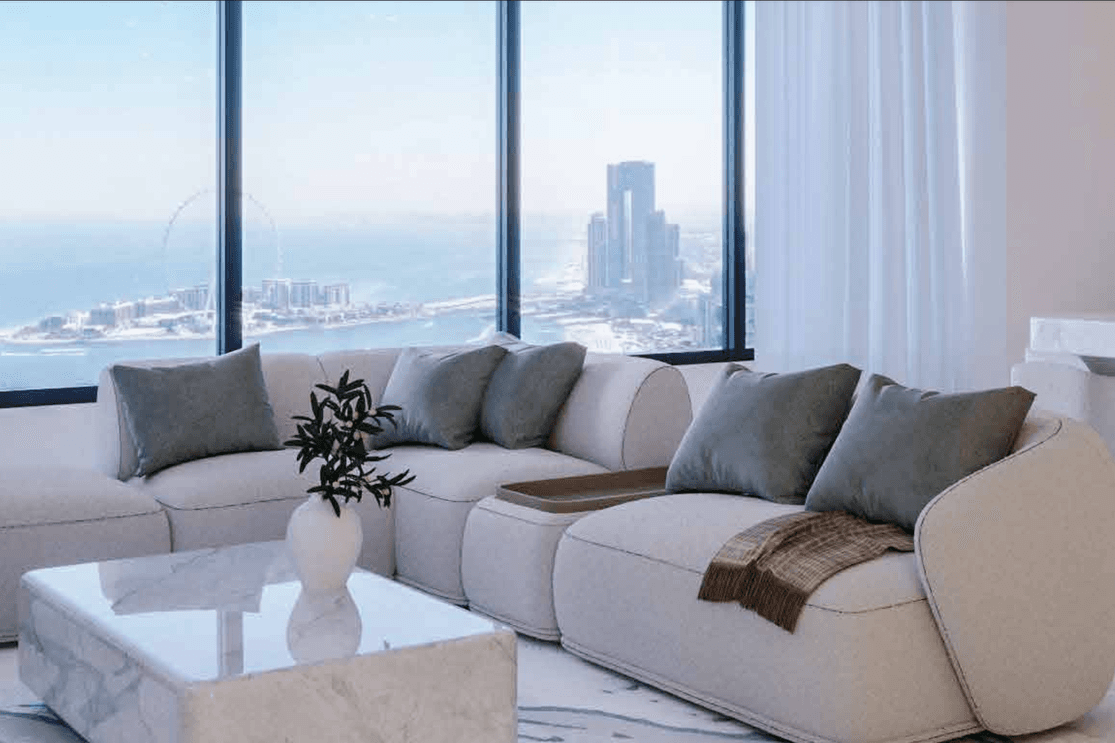Modern living room with a curved beige sofa, green cushions, and marble table. Large windows offer a city skyline and ocean view.