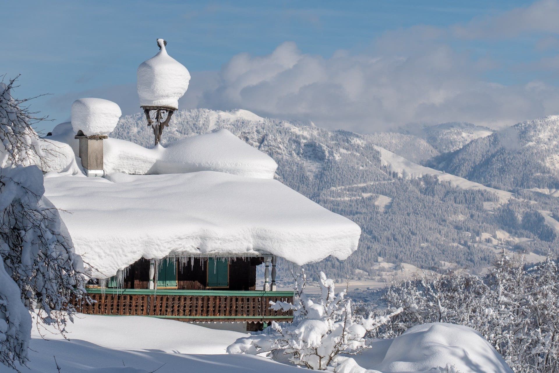 Ein Chalet mit tief verschneitem Dach vor einer atemberaubenden Berglandschaft – eine exklusive Ski in Ski out Immobilie in Tirol für Wintersportbegeisterte.