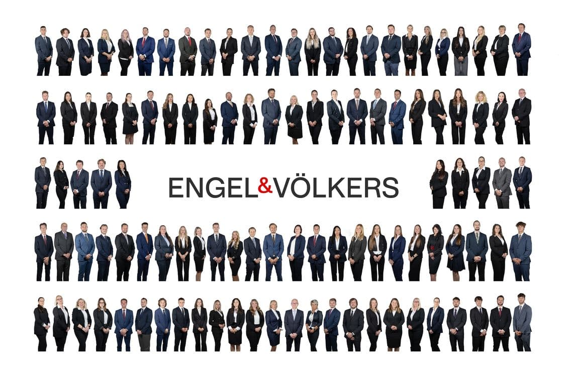 Group photo of the entire Engel & Völkers team. Dozens of men and women in business suits stand in several horizontal rows against a white background, with the Engel & Völkers logo prominently displayed in the center.