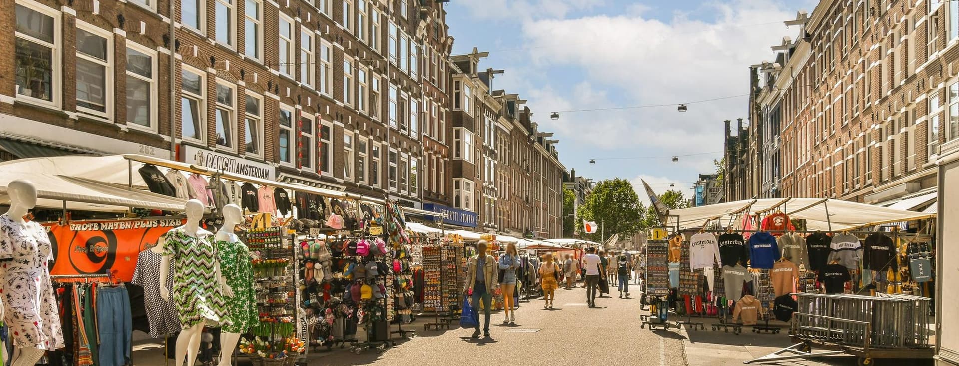 Street view of Albert Cuyp Market in Amsterdam, Netherlands. Vendors sell clothing and souvenirs from stalls. People walk along the street.