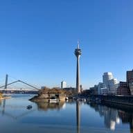 Düsseldorfer Skyline mit dem Rheinturm und moderner Architektur, die sich im Wasser spiegelt.