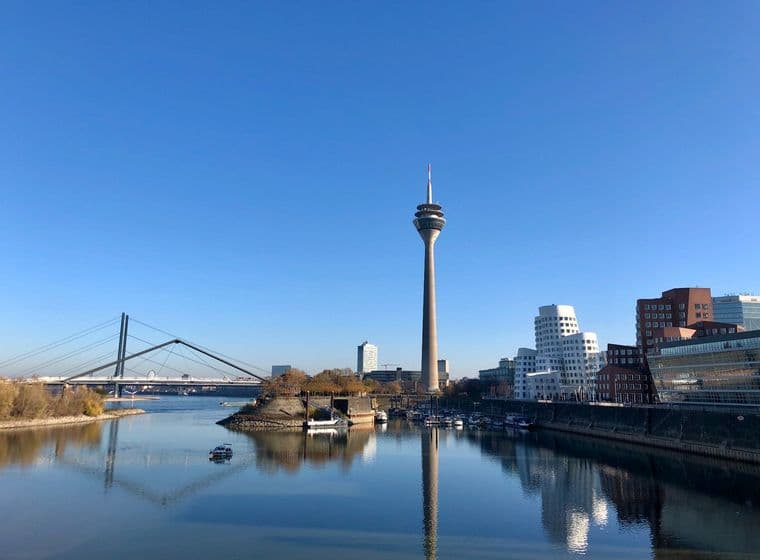 Düsseldorfer Skyline mit dem Rheinturm und moderner Architektur, die sich im Wasser spiegelt.