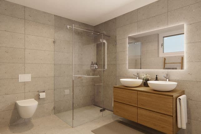 Modernes Badezimmer mit beige gefliesten Wänden, einer Glasdusche, einer wandhängenden Toilette, einem Waschtisch aus Holz mit zwei Waschbecken und einem beleuchteten Spiegel.