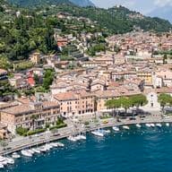 Luftaufnahme einer Stadt am See mit einem Yachthafen, umgeben von üppigen grünen Hügeln und Bergen unter einem klaren Himmel.