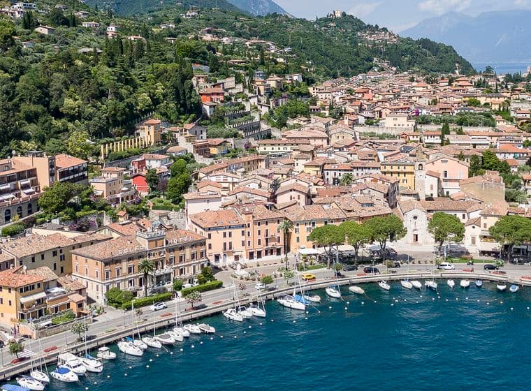 Luftaufnahme einer Stadt am See mit einem Yachthafen, umgeben von üppigen grünen Hügeln und Bergen unter einem klaren Himmel.