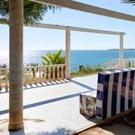 Banca fija vacía en el paseo de Punta Prima con vista al mar y palmeras.