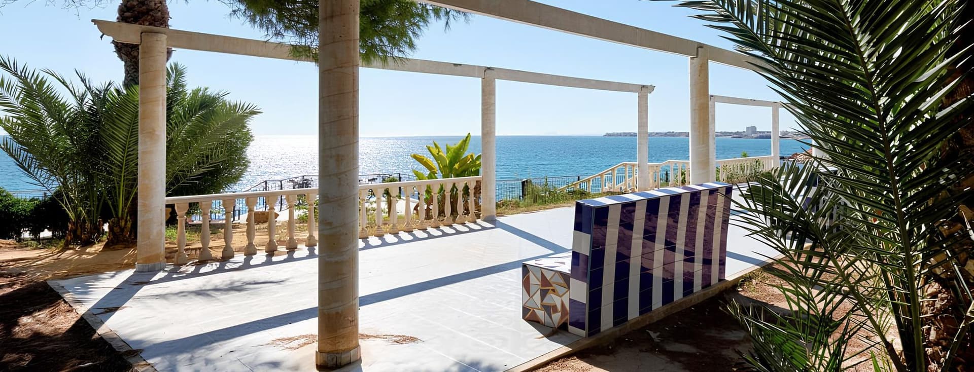 Banca fixa buida al passeig de Punta Prima amb vista al mar i palmeres.