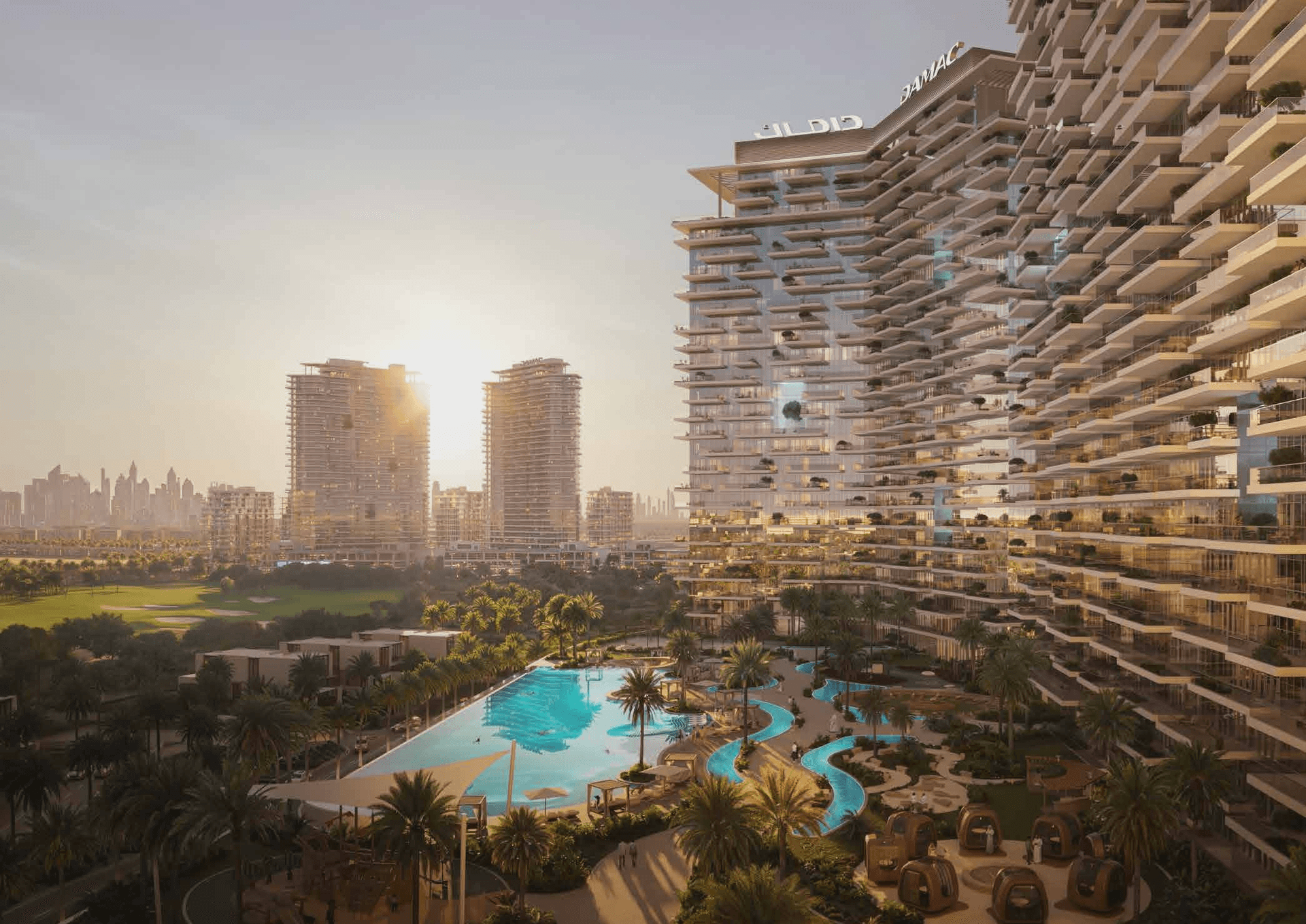 Modern high-rise buildings with balconies, overlooking a large swimming pool and lush gardens at sunset; city skyline in the background.