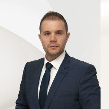 Φωτογραφία πορτρέτου ενός άνδρα με μπλε κοστούμι και γραβάτα σε λευκό φόντο.