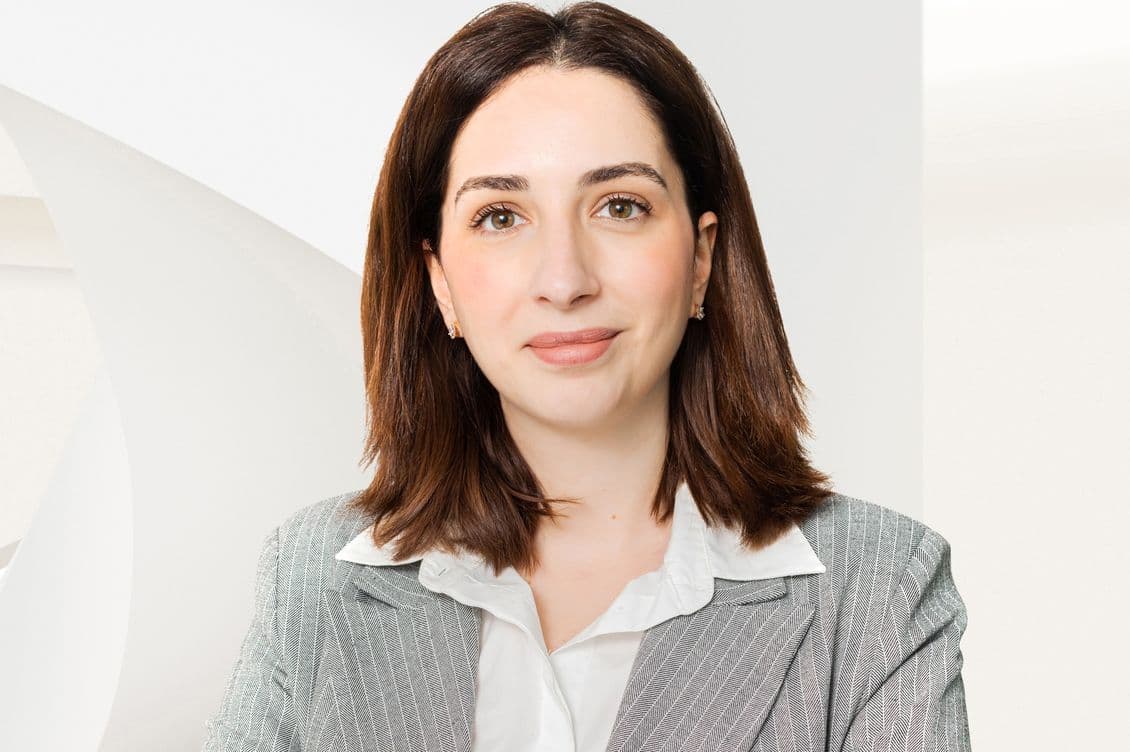 A headshot of a woman with brown hair wearing a gray blazer and white shirt.
