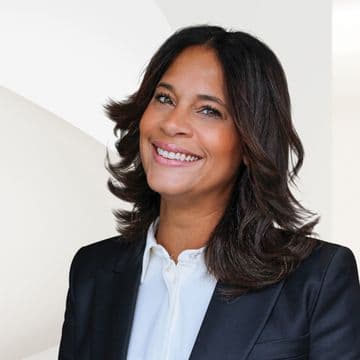 A smiling woman with dark hair, wearing a black blazer and white shirt, poses against a white background.