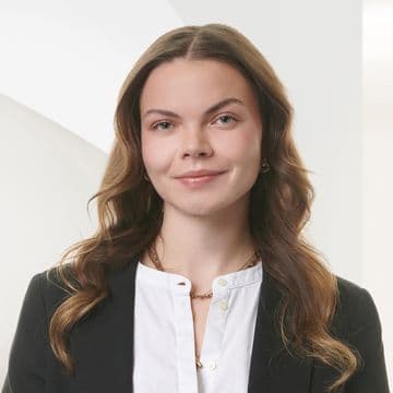 Smiling woman with long wavy hair in a black blazer and white shirt against a white background.