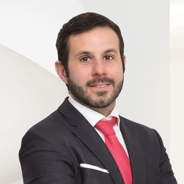uomo carnagione chiara capelli e barba scura occhi scuri con giacca grigia camicia bianca e cravatta rossa