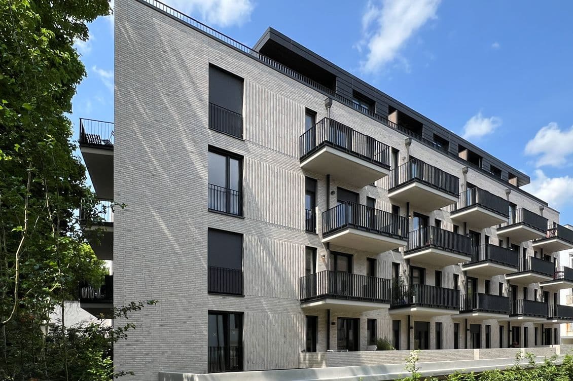 Neubaufassade von Wohnkomplex mit weißer Fassade und schwarzen Balkonen mit Gitterstäben