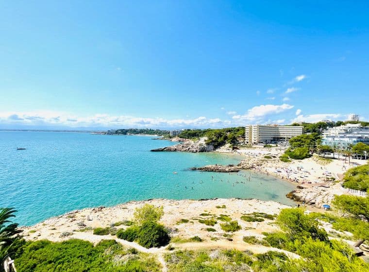 Imagen de la playa en la Costa Dorada hecha por el equipo de Engel & Volkers. Se ve el agua cristalina, y algunos edificios en la costa.