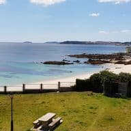 Vista de la platja d'Areas amb Sanxenxo al fons. Es veu un parc amb una taula, la platja al mig i Sanxenxo a l'horitzó.
