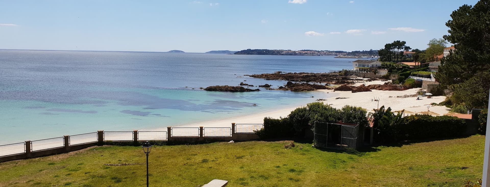 Vista de la platja d'Areas amb Sanxenxo al fons. Es veu un parc amb una taula, la platja al mig i Sanxenxo a l'horitzó.
